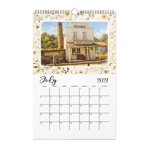 May include: A 2021 wall calendar for the month of July featuring a watercolor illustration of a historic building labeled ROOMS and WALNUT GROVE POST OFFICE, with a HANS DORFLER BLACKSMITH sign, surrounded by a floral border and wire binding.