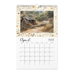 May include: A wall calendar for April 2021 featuring a painting of a rustic wooden grain building with a sign reading GRAIN. The border is decorated with a pattern of small yellow flowers and green leaves on a cream background with a metal spiral binding.