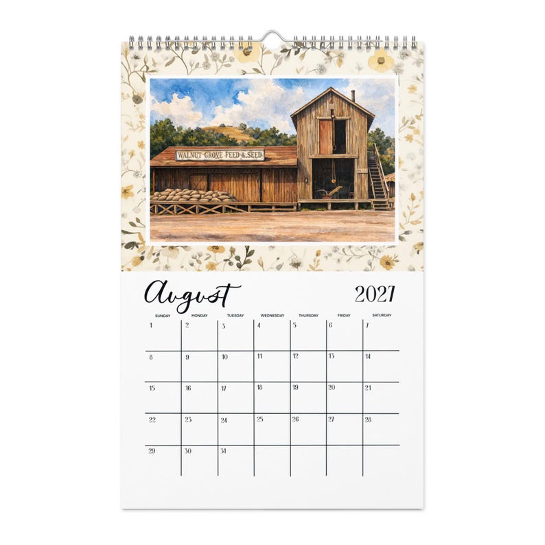 May include: A wall calendar for August 2021 featuring a watercolor illustration of a wooden building labeled Walnut Grove Feed & Seed. The scene includes a stack of burlap sacks, a wooden staircase, and a blue sky with clouds, framed by a floral border.