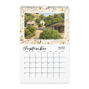 May include: A wall calendar for September 2021 featuring a top section with a floral border and a painting of a rural town scene with buildings labeled 'Eleanor's Mercantile' and 'Hanson Lumber Co.' The bottom section displays a standard grid calendar.