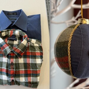 Op de afbeelding: Twee geruite overhemden, een blauwe en een groene, rode en witte, liggen gevouwen op een wit oppervlak. Een blauwe en groene geruite kerstbal met een gouden touwversiering en een blauwe knoop hangt aan een witte tak.