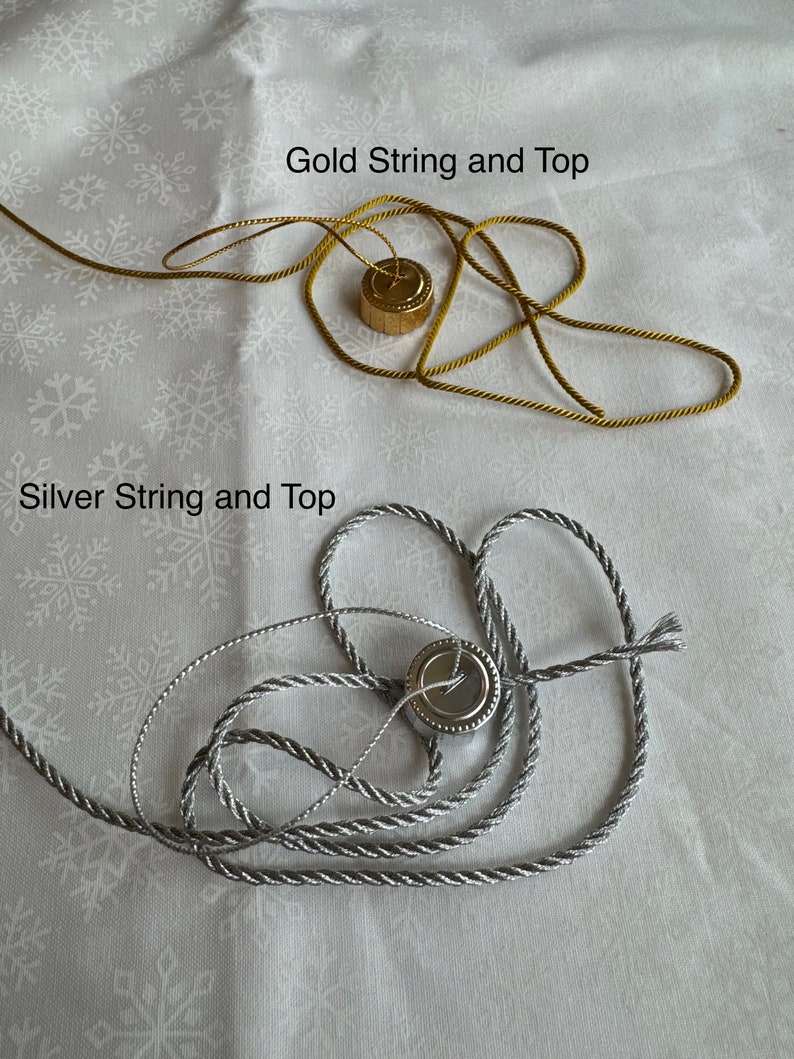 Op de afbeelding: Twee spoelen touw, een gouden en een zilveren, met metalen toppen. Het touw is gedraaid en heeft een touwachtige textuur.