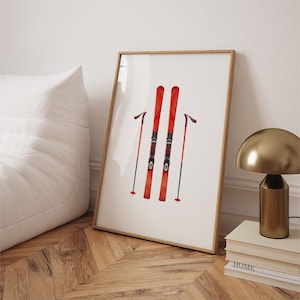 Pode incluir: Uma impressão emoldurada de um par de esquis vermelhos com fixações pretas e dois bastões de esqui pretos sobre um fundo branco.