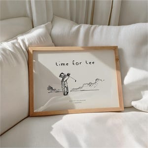 May include: A framed print with a light wood frame. The print features a black and white sketch of a golfer swinging a club, with the words "time for tee" above the image. The words "Sketchy Collection, Timeprints" are below the image.
