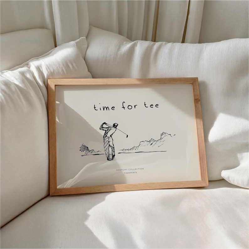 May include: A framed print with a light wood frame. The print features a black and white sketch of a golfer swinging a club, with the words "time for tee" above the image. The words "Sketchy Collection, Timeprints" are below the image.