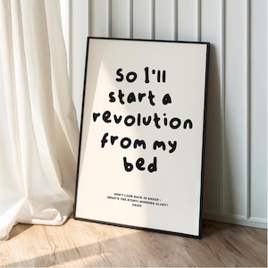 May include: A framed art print with the text "So I'll start a revolution from my bed" in black on a white background. The print includes the quote "Don't Look Back in Anger" and the band Oasis.