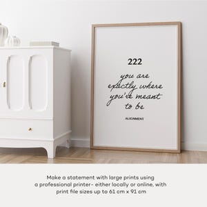 May include: A framed print with a white background and black text that reads "222 you are exactly where you're meant to be ALIGNMENT". The print is framed in a light wood frame and is sitting on a white surface.