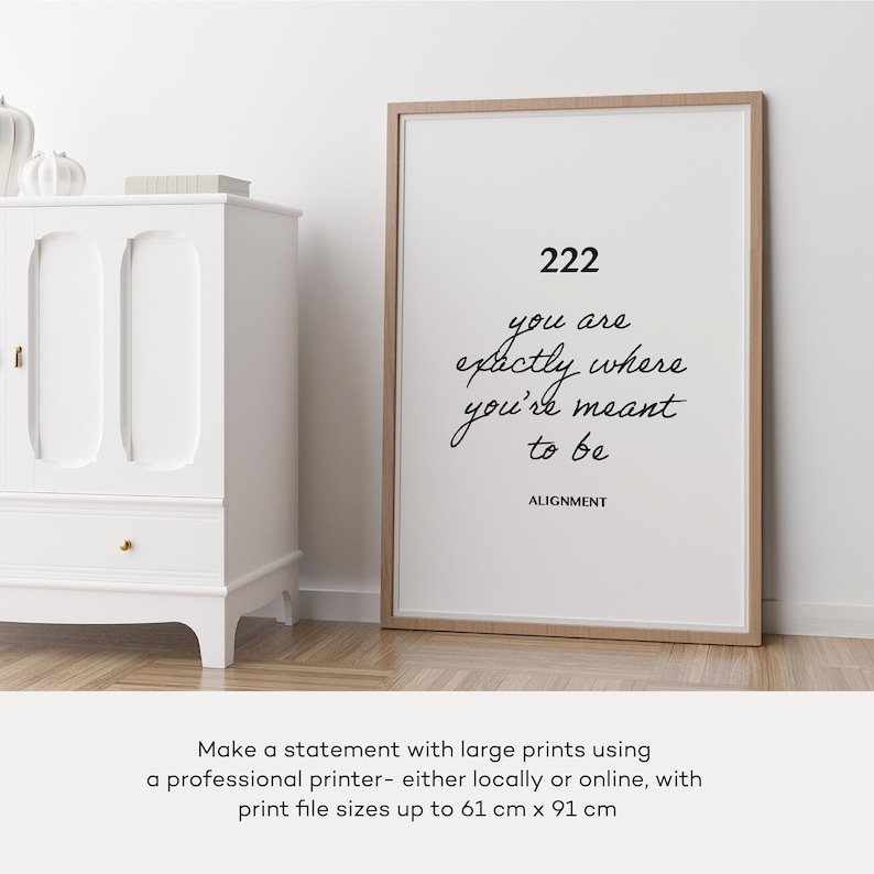 May include: A framed print with a white background and black text that reads "222 you are exactly where you're meant to be ALIGNMENT". The print is framed in a light wood frame and is sitting on a white surface.