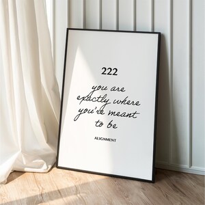 May include: A black framed poster with white background and black text that reads "222 you are exactly where you're meant to be ALIGNMENT".