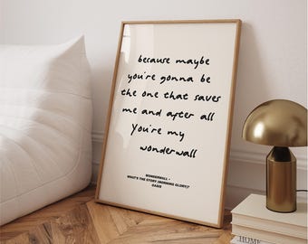 May include: A framed print with the lyrics "because maybe you're gonna be the one that saves me and after all You're my wonderwall" in black script. The print is in a light wood frame, leaning against a white wall. A gold lamp and books are nearby.