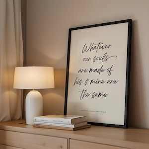 Może przedstawiać: Oprawiony wydruk z cytatem "Whatever our souls are made of, his & mine are the same" czcionką. Biała lampa stołowa i stos książek na drewnianej komodzie. Wydruk jest w czarnej ramie.