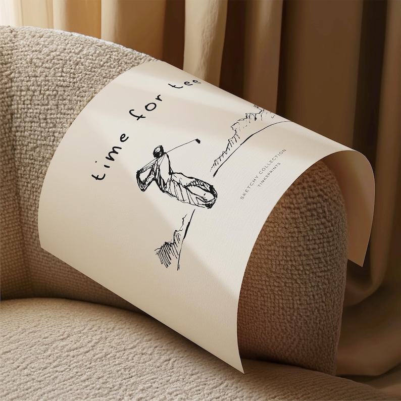 May include: A cream-colored print with a black sketch of a golfer swinging a club, with the words "time for tee" and "Sketchy Collection TINKPRINTS". The print is wrapped around a beige upholstered armrest.