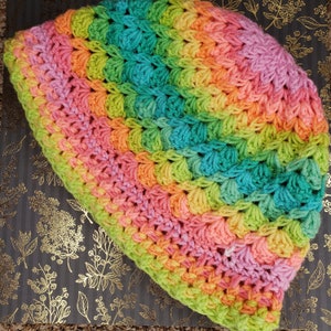 Può includere: Un berretto all'uncinetto fatto a mano con i colori dell'arcobaleno. Il cappello presenta un motivo a punto strutturato e una sfumatura di rosa, arancione, giallo, verde e blu. Questo berretto accogliente è un accessorio elegante.