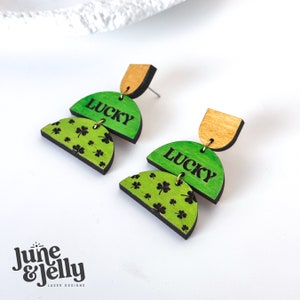 May include: A pair of green and gold wooden earrings with a shamrock pattern and the word "LUCKY" on each earring.