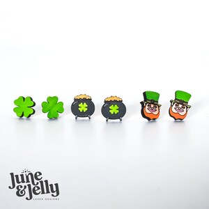 Op de afbeelding: Een set van zes houten oorbellen met een St. Patrick's Day thema. De oorbellen zijn groen, zwart en goud en bevatten klavertjesvier, potten met goud en kabouters.