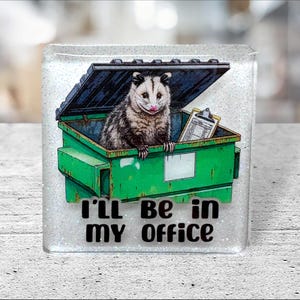 Könnte beinhalten: Quadratisches, glitzerndes Bild mit einem Cartoon-Opossum in einem grünen Müllcontainer mit Klemmbrett. Das Opossum hat eine rosa Nase und den Text "I'll be in my office".