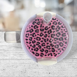 Pode incluir: Base de copo com estampa de leopardo rosa e preto com canudo transparente e borda branca. A base do copo é redonda e tem um acabamento brilhante. O design é um padrão arrojado e atraente.