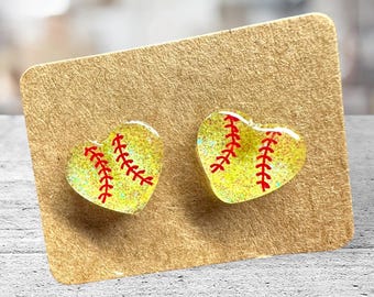 Op de afbeelding: Een paar hartvormige oorbellen met een geel en rood softbalontwerp. De oorbellen bevinden zich op een bruine kaart.