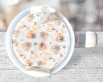 May include: White ceramic mug with a lid and a straw. The lid has a pattern of orange and brown pumpkins with bows and stars on a white background.