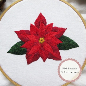 May include: A hand-stitched poinsettia flower in a wooden embroidery hoop. The flower has vibrant red petals and a yellow centre, with green leaves. The text "PDF Pattern & Instructions" is displayed in a pink circle.
