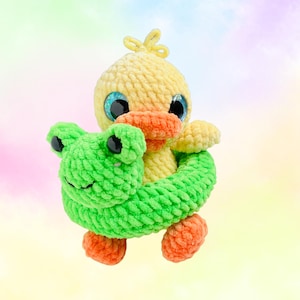 May include: A handmade yellow crochet duck with orange feet and beak, and large blue eyes. The duck is embracing a green crochet frog. The toy is soft and plush, perfect for a child's room or as a decorative item.