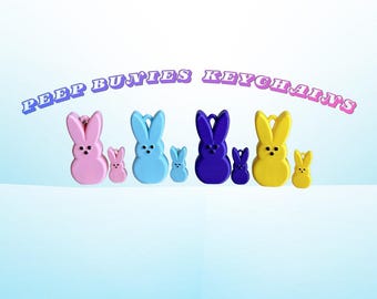 May include: A collection of colorful bunny keychains in pink, blue, purple, and yellow. Each keychain features a large bunny and a smaller bunny. The text "PEEP BUNNIES KEYCHAINS" is arched above the keychains.