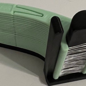 May include: A black plastic holder with a stack of green plastic razor blades. The holder has a slot for the blades to be inserted and a mechanism to hold them in place.
