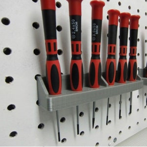 May include: A gray plastic wall-mounted organizer with six red and black screwdrivers. The screwdrivers are labeled with the text "2.4x50 SNCM" and "3.0x50 SNCM".