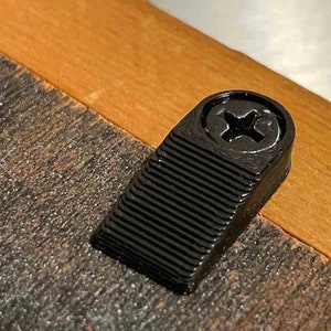 May include: Black plastic screw with a star-shaped head, mounted on a wooden surface.