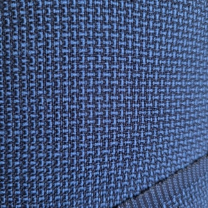 May include: Close-up of a blue fabric with a woven pattern. The fabric has a subtle texture and a dark blue color.
