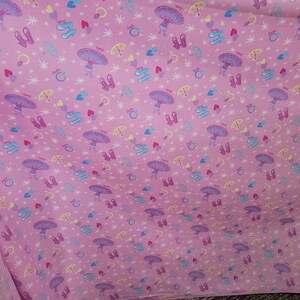 May include: Pink fabric featuring a repeating pattern of ballet shoes, umbrellas, hearts, stars, and rings. The ballet shoes are purple and blue, the umbrellas are purple and yellow, and the hearts are red and blue.