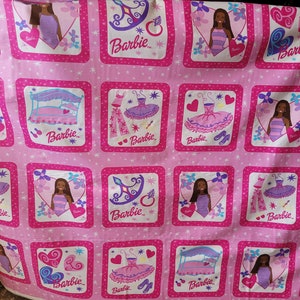May include: Pink fabric featuring repeating square patterns with Barbie illustrations. Each square contains a Barbie doll, a bed, a dress, or accessories. The word "Barbie" is written in a stylized font within each square.