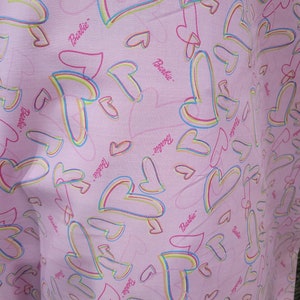 May include: Pink fabric with a repeating pattern of multi-colored hearts and the word "Barbie" throughout.