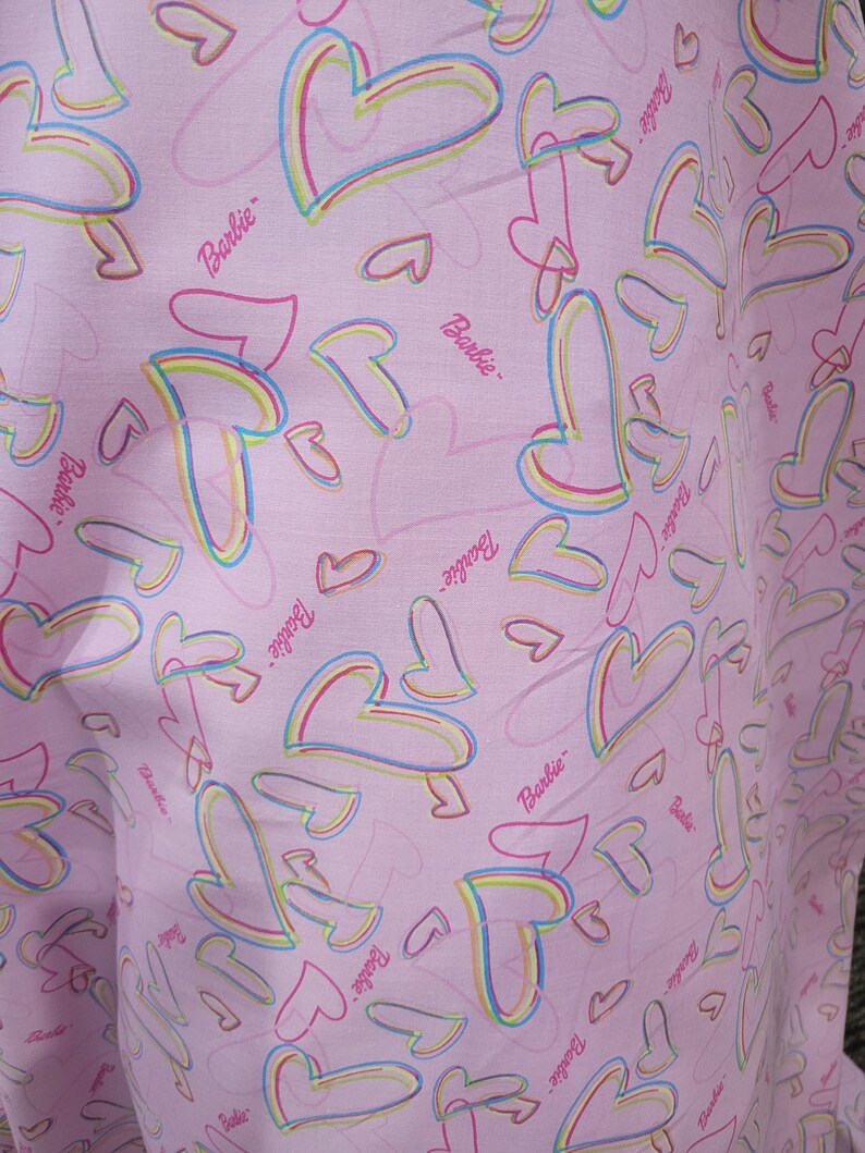 May include: Pink fabric with a repeating pattern of multi-colored hearts and the word "Barbie" throughout.