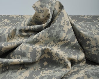 Könnte beinhalten: Digitales Tarnmustergewebe in Grau-, Beige- und Beigetönen. Der Stoff ist drapiert und zeigt Falten und Texturen. Das Muster besteht aus kleinen, pixeligen Quadraten, die ein militärisch inspiriertes Design erzeugen. Das Material scheint ein mittelschwerer Stoff zu sein.