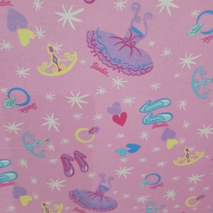 May include: Pink fabric with a repeating pattern of ballet-themed illustrations. The design includes ballet shoes, tutus, tiaras, hearts, rings, and stars. The word "Barbie" is printed on the fabric.