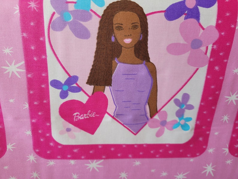 May include: Pink fabric featuring a Barbie doll illustration. The doll is inside a heart-shaped frame, surrounded by flowers. The word "Barbie" is written on a heart. The background has a pattern of stars and stripes.