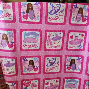 May include: Pink fabric featuring repeating square patterns with Barbie-themed illustrations. Each square contains a Barbie doll image, a heart, and the Barbie logo. Other squares show a bed, a tutu, and a ring.