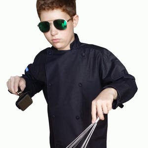 May include: A black chef's coat with a double-breasted front and a high collar. The person is wearing green-tinted aviator sunglasses and holding a whisk and a meat tenderizer.