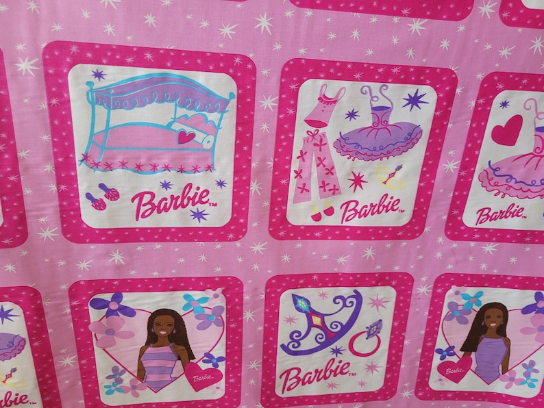 May include: Pink fabric with repeating square patterns featuring Barbie illustrations. Each square has a pink border and a white interior with images of Barbie, a bed, clothing, and accessories. The background is a lighter pink with white starbursts.