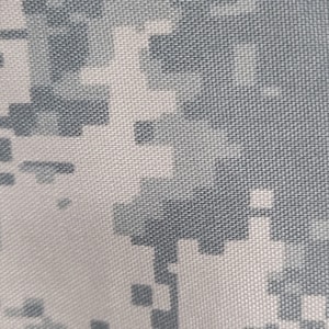 May include: Close-up of a fabric with a digital camouflage pattern. The design features a pixelated arrangement of gray and white squares, creating a textured appearance. The fabric's weave is visible, adding to the overall detail.