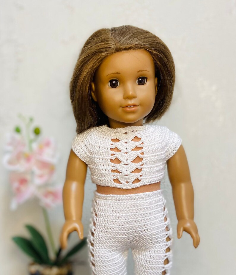 Op de afbeelding: Een wit gebreid crop top en broek set voor een pop. De top heeft een uitgesneden ontwerp en de broek heeft een zijsplit detail.
