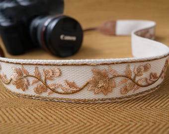 Correa para cámara DSLR/sin espejo con bordado floral en oro cálido y extremos de cuero color canela. Accesorio de fotografía ideal como regalo.