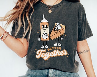 Op de afbeelding: Een donkergrijs T-shirt met een afbeelding van een slagroomspuitbus en een stuk taart die elkaar de hand vasthouden. De tekst "Better Together" is onder de afbeelding gedrukt.