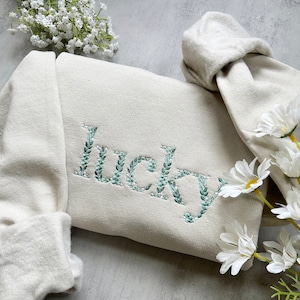 May include: A cream coloured sweatshirt with the word "lucky" embroidered in green leaves on the front.