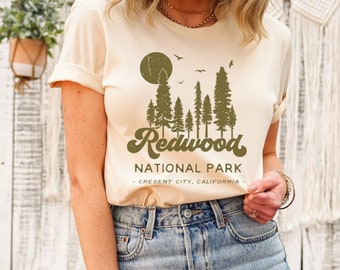 May include: A cream colored t-shirt with a green graphic of a forest scene and the text "Redwood National Park - Crescent City, California".