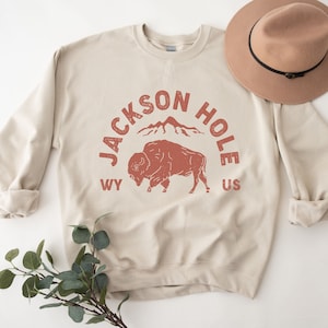 May include: A beige sweatshirt with a red graphic print of a bison, mountains, and the text "JACKSON HOLE WY US".