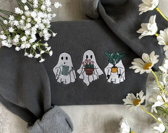 Op de afbeelding: Een donkergrijs sweatshirt met geborduurde witte geesten die planten en een gieter vasthouden. Het sweatshirt heeft een grijze fleecevoering aan de manchetten en zoom.