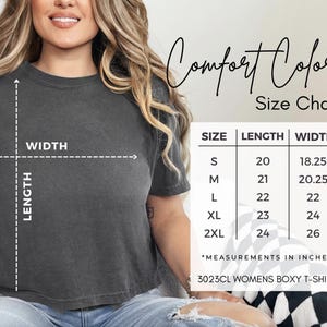 Pode incluir: Uma t-shirt boxy Comfort Colors cinza escuro com uma tabela de tamanhos. A tabela mostra as medidas em polegadas para os tamanhos S a 2XL. O texto "Comfort Colors" e "Size Chart" tamb&eacute;m s&atilde;o vis&iacute;veis.