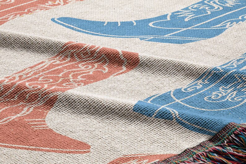 May include: A woven throw blanket with a cream background and a repeating pattern of blue and red cowboy boots. The blanket has a fringe border.